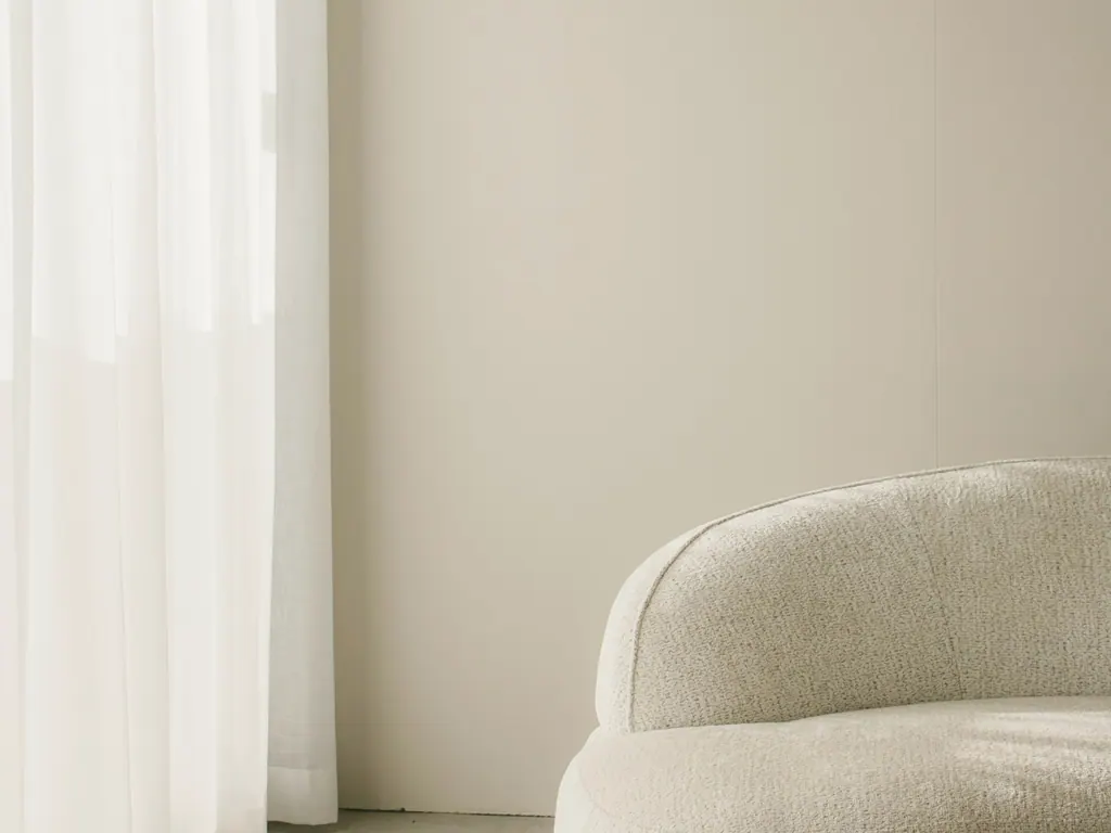 Sofá curvo de bouclé off-white junto a cortinas translúcidas, em uma sala clara.